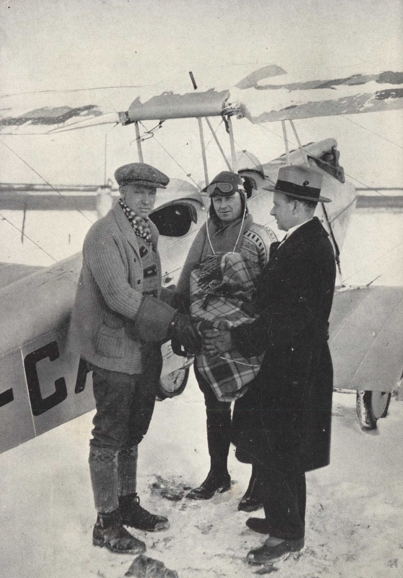 Three men standing in front of a open cockpit biplane in the winter